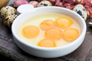 raw and open quail eggs in porcelain bowl, on rustic wood