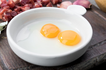 raw and open quail eggs in porcelain bowl, on rustic wood