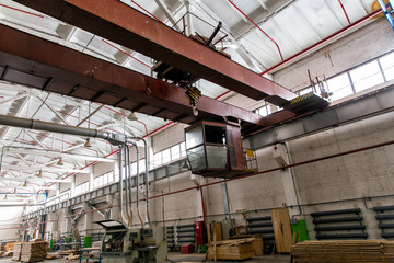 Overhead cranes with a crane operator cabin and hooks in a multi-span metal frame workshop. Steel landing pad.