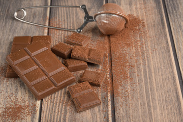 Milk chocolate with cocoa powder. On a wooden texture. C blank space for inscription or advertising.