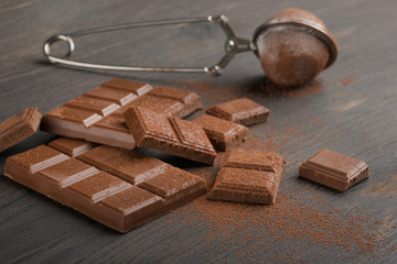 Milk chocolate with cocoa powder. On a wooden texture. C blank space for inscription or advertising.