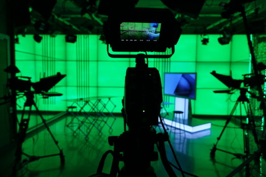 Silhouette of a digital video camera in front of a green screen.