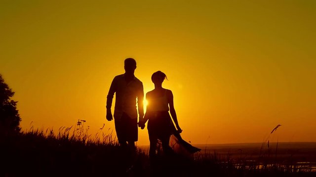 Loving couple - young man and beautiful girl walking at sunset meadow - silhouette