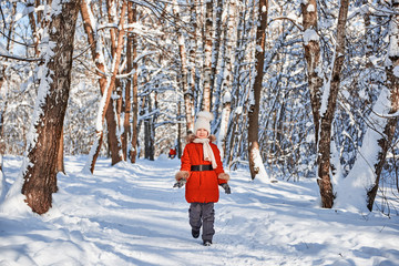 Girl in red coat, knitted ivory scarf and hat walking on winter snowy forest background