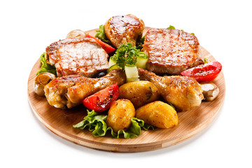 Grilled steak and drumsticks with potatoes on cutting board