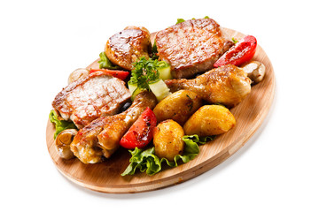 Grilled steak and drumsticks with potatoes on cutting board