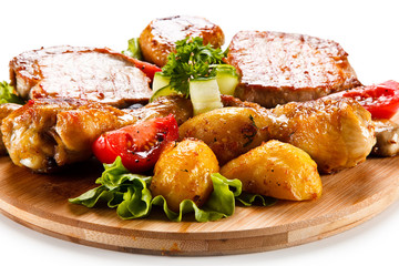 Grilled steak and drumsticks with potatoes on cutting board