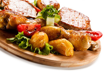 Grilled steak and drumsticks with potatoes on cutting board