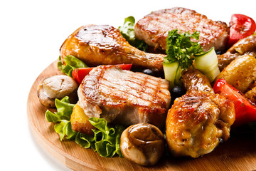 Grilled steak and drumsticks with potatoes on cutting board