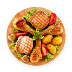 Grilled steak and drumsticks with potatoes on cutting board