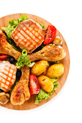 Grilled steak and drumsticks with potatoes on cutting board