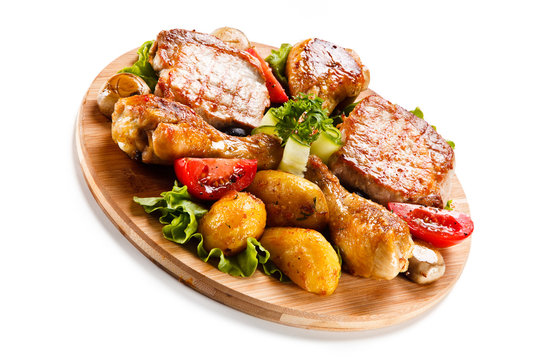 Grilled steak and drumsticks with potatoes on cutting board