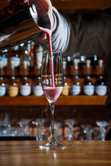 The barman in the bar pours an alcoholic cocktail into a glass with a powerful stream, not afraid to spill on the table.