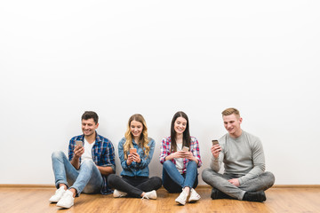 The four happy people sit on the floor and phone on the white background