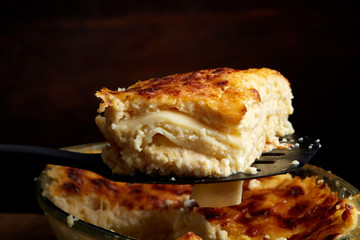 A piece of lasagna cooked in a glass pan over vintage wooden background, top view, close-up, selective focus