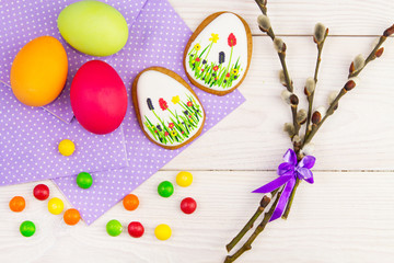 Easter background with Easter eggs and a willow twig. Easter gingerbread, eggs and willow twig on white wooden background. Easter Trend colors