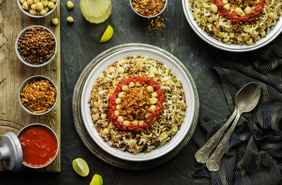 Arabic cuisine; Traditional Egyptian food:Delicious Kushary or Koushari of rice,pasta,chickpeas,lentils,crispy fried onions,fresh lemon and tomato garlic sauce on a plate.Top view with close-up
