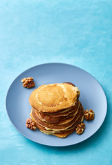 Pile of homemade pancakes with walnuts on blueish plate over blue background, selective focus
