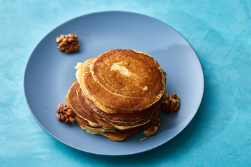 Pile of homemade pancakes with walnuts on blueish plate over blue background, selective focus