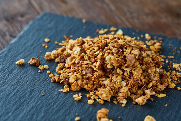 Pile of healthy granola on black stony board over vintage wooden background, top view, close-up, selective focus