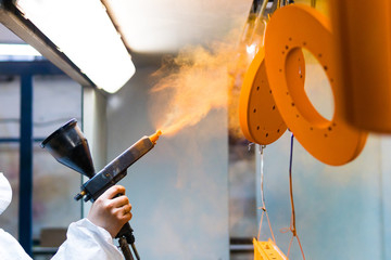 Powder coating of metal parts. A woman in a protective suit sprays powder paint from a gun on metal...