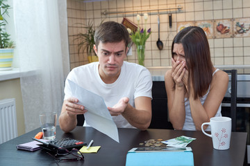 a young couple sitting in the kitchen planning and analyzing the family budget. Financial difficulties, negative emotions