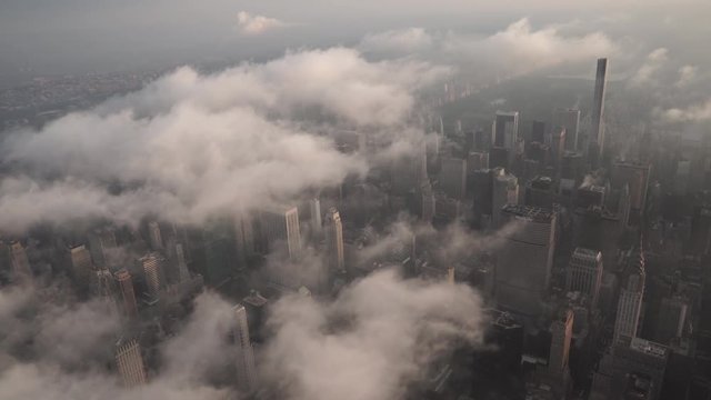 New York City aerial view flying over Midtown Manhattan skyscrapers under fog and low level clouds at sunrise.