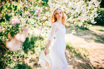 Fine art portrait of young blonde girl in white elegant dress in summer blooming lilac garden....