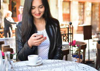 Attractive woman in a street cafe with a phone. A girl at a lunch break drinks coffee and communicates through the messenger with her smartphone. The Internet. Message.