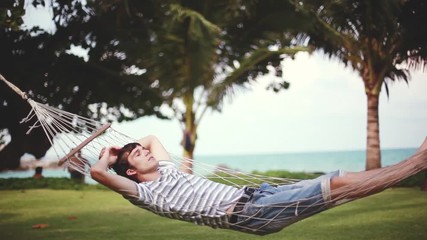 Young handsome man relaxing on hammock on beautiful tropical beach. Vacation concept. 1920x1080 - Powered by Adobe