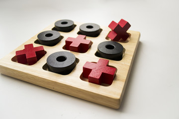 Wooden tic tac toe game on white blurred background. Red crosses and black noughts