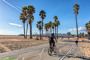 Men biking and running on Santa Monica bike path - obrazy, fototapety, plakaty