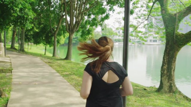Young overweight woman jogging in the park. Concept of struggle against excess weight. Slow motion.