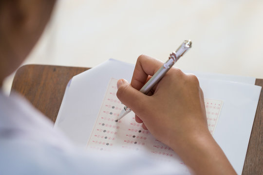 Students hand testing doing examination with pen drawing selected choice on answer sheets in school exams, blur pupils college background. Education system tests concept.