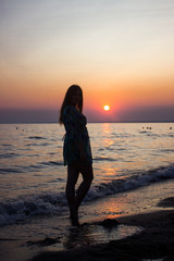 Fototapeta premium silhouette of a young, slender girl in the background of the setting sun on the beach, looking at the sunset