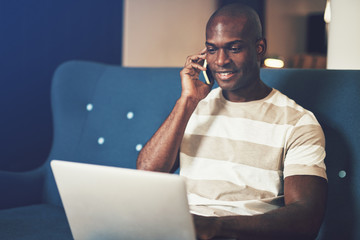 Young African entrepreneur talking on his cellphone and working online