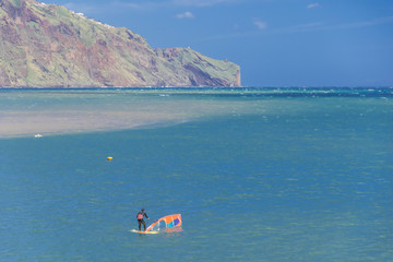 Picturesque landscape with a rock in the backround and a water sports enthusiast, windsurfer with...