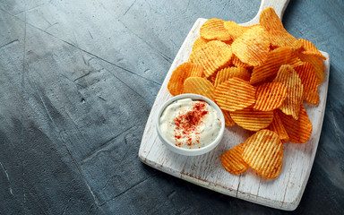 Potato chips, snack crisps with red paprika and white dip sauce on white board.