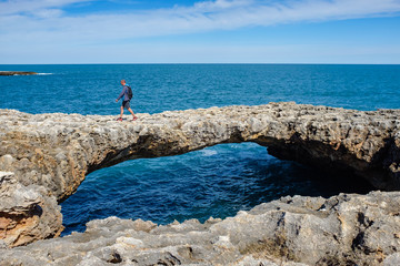 Man walks on a natural rock arch along the coastline of Polignano. Apulia, Italy