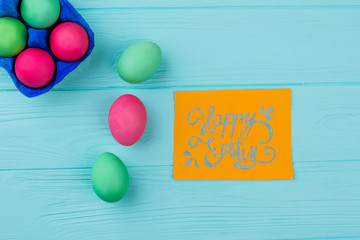 Easter dyed eggs on wooden background. Easter festive eggs, top view. Handwritten Easter greeting card.
