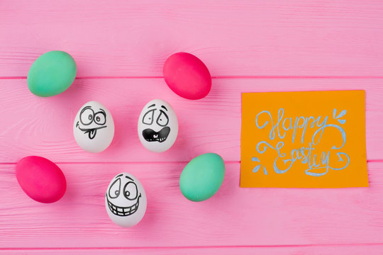 Happy Easter card and funny eggs. Colorful Easter eggs on pink wood. Easter holidays concept.