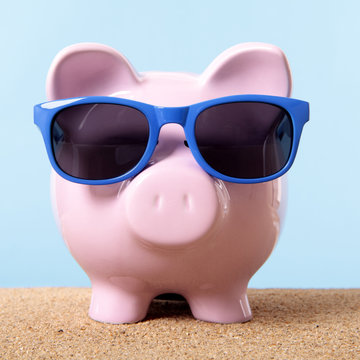 Pink piggy bank or piggybank one single wearing sunglasses on a sandy summer beach retirement vacation holiday money saving plan planning photo