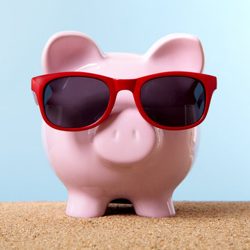 Pink piggy bank or piggybank one single wearing sunglasses on a sandy summer beach retirement vacation holiday money saving plan planning photo