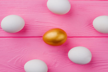 Chicken eggs on pink wooden background. Group of white and one golden egg on wood plank. Preparation for Easter holidays.