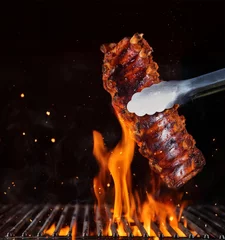 Wall murals Grill / Barbecue Pork ribs over flaming grill grid, isolated on black background.