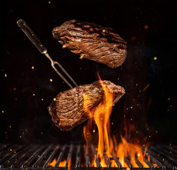 Flying beef steaks over grill grid, isolated on black background