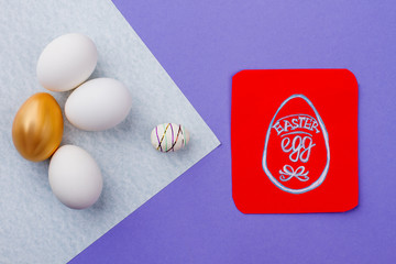 Easter composition with eggs and card. Red paper card with picture of Egg drawn by child. Golden egg among white eggs. Concept of happy Easter.