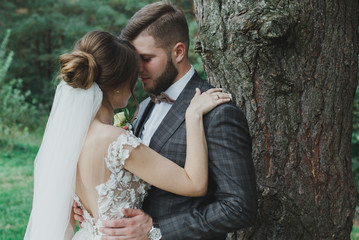 Beautiful wedding couple in the forest. The bride with tulle veil and open low back elegant dress...