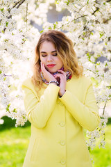 A young woman dressed in a fashionable yellow coat in a flowering park