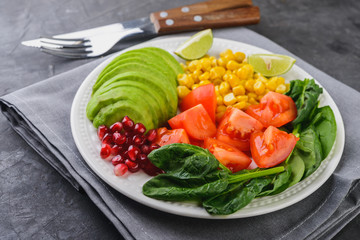 Fresh avocado salad with tomatoes, pomegranate,  spinach, lime and corn on dark  background  Healthy food concept.